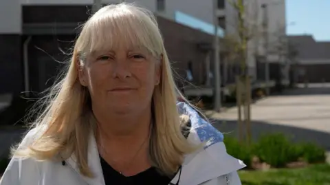 Karen Quinn. Tiene una edad media, tiene un cabello rubio de bob y usa una bata blanca. 